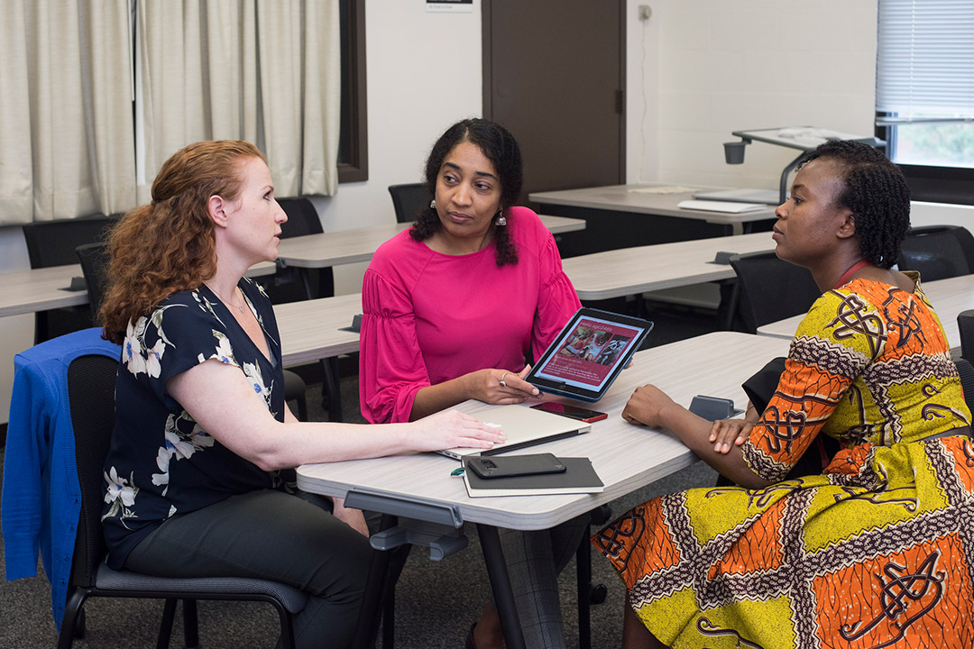 Three women discuss app on tablet.