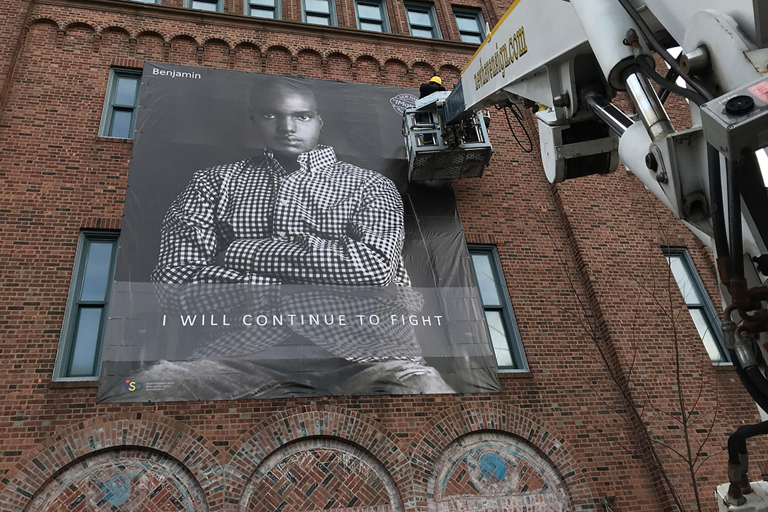 Giant portrait of young man being installed on exterior brick wall.