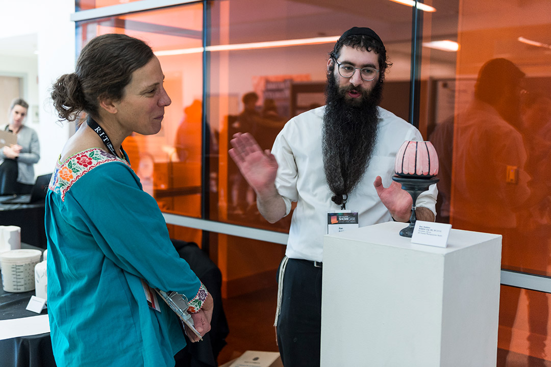 Student explains ceramic piece to visitor.