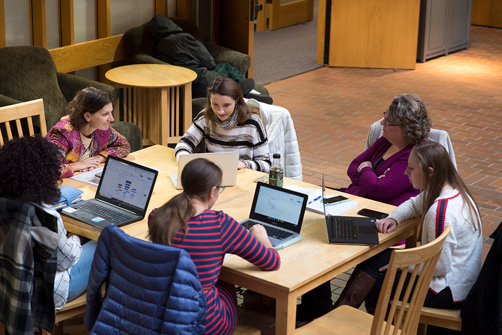 Students and faculty sit at table with laptops.