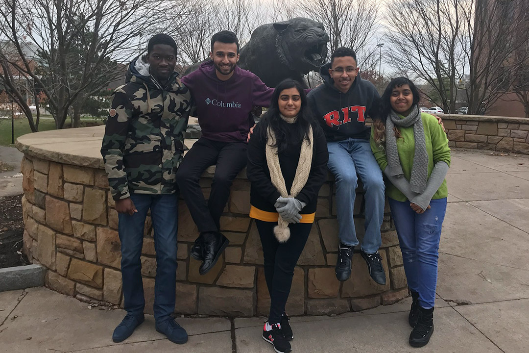 Group of students stands and sits near statue of tiger.