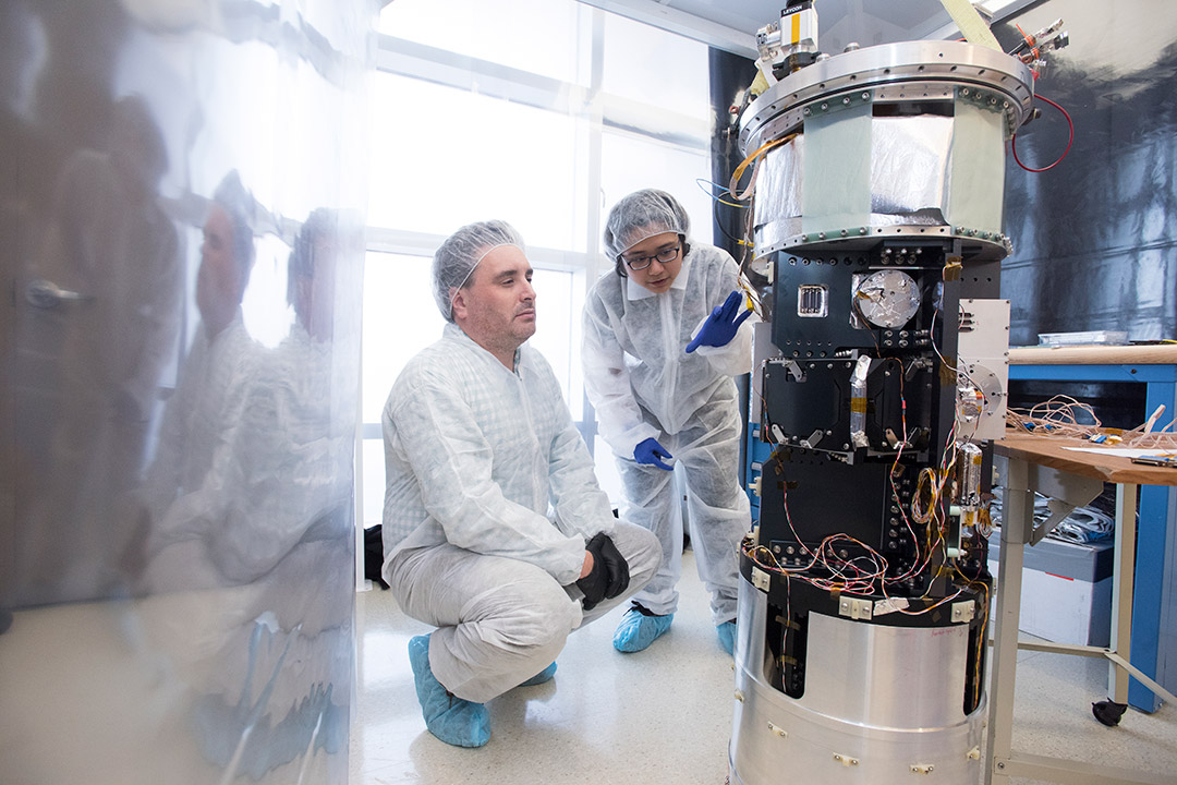 Two researchers wearing cleansuits work on detector equipment.