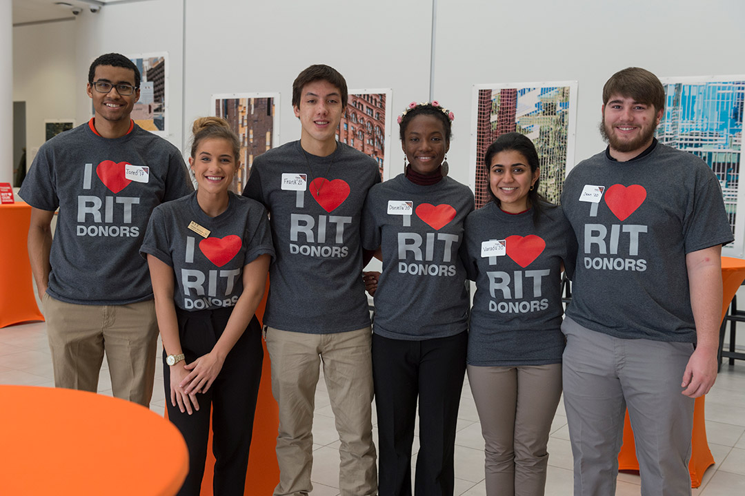 group of six students standing together wearing gray T-shirts that say I heart RIT donors.