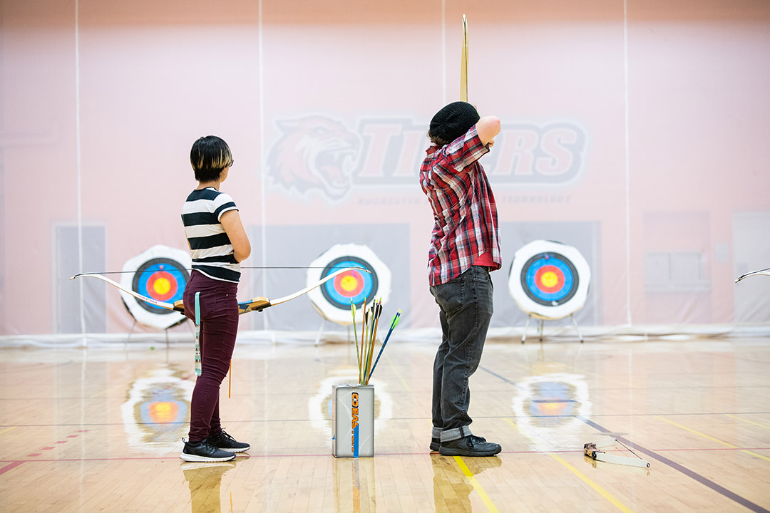 two students in archery class aim arrows at targets.