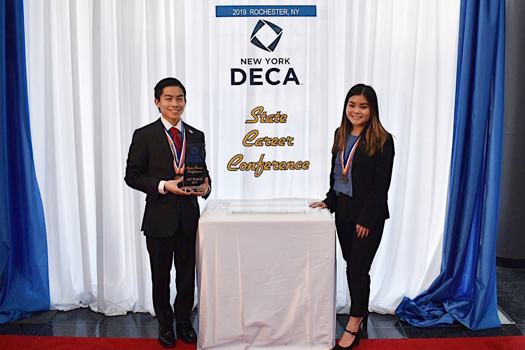 two students wearing medals pose with award.