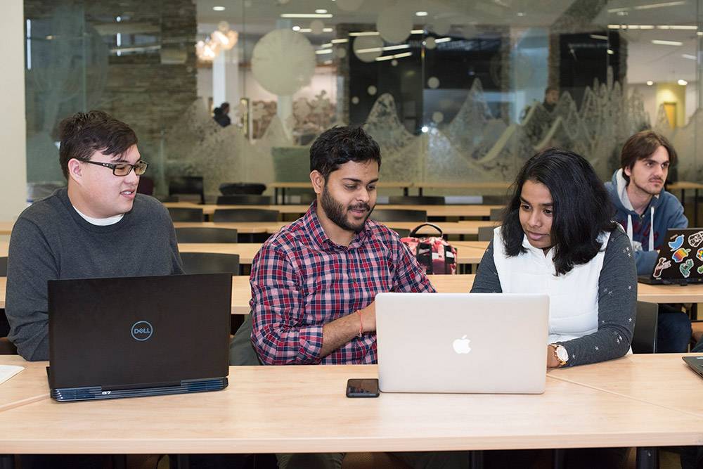 three students at table on laptops.