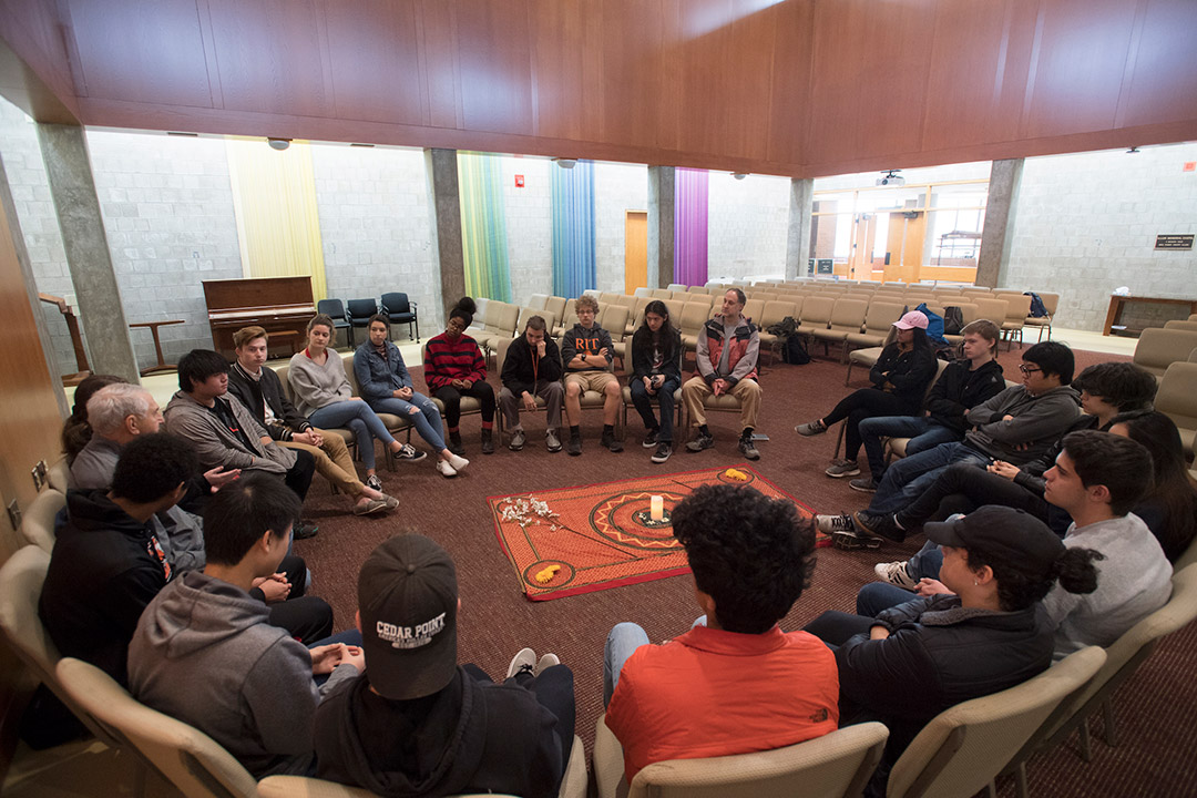 Large group of students sits in circle having discussion.