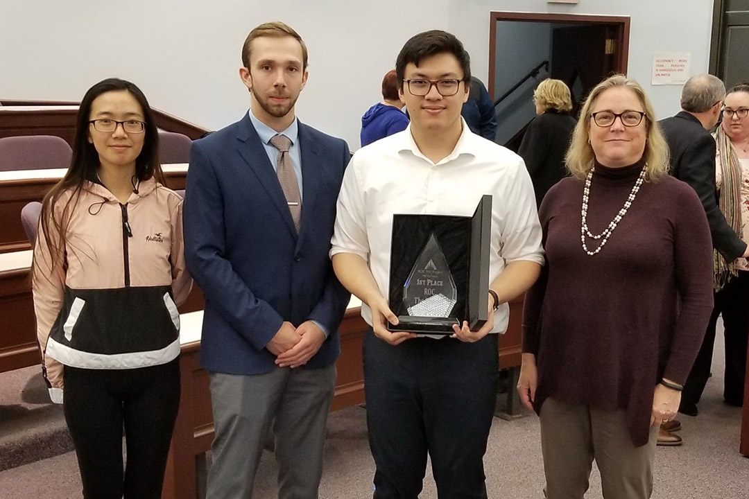 three students and volunteer mentor standing with award.