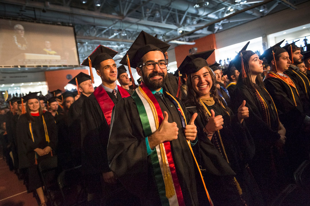 Graduting students wearing caps and gowns give thumbs-up.