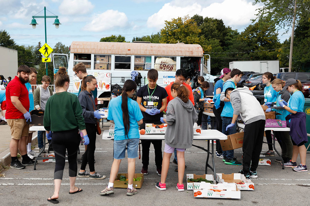 students crowding around tables of produce at a public market.