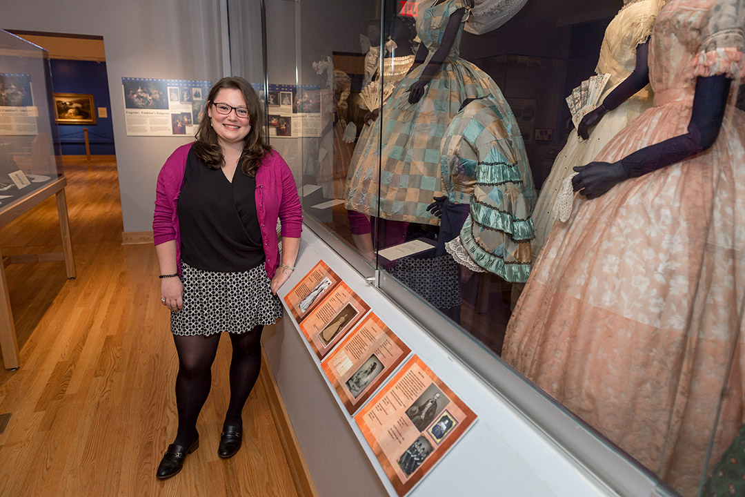 student posing with museum exhibit of women's dresses.