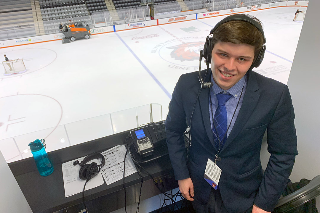 student wearing headset in press box in ice arena.