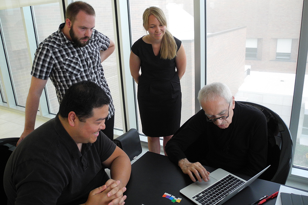 Massimo Vignelli works with young design professionals who look on as he demonstrates on his computer.