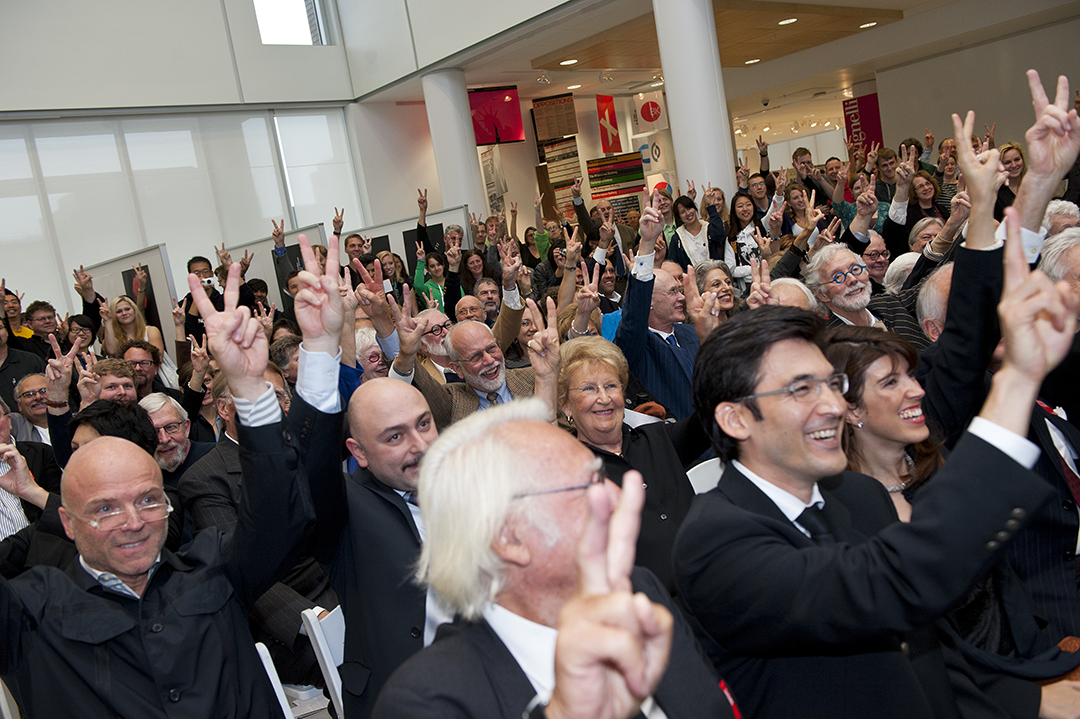 A crowd makes a "V" with their fingers to celebrate the opening of the Vignelli Center.