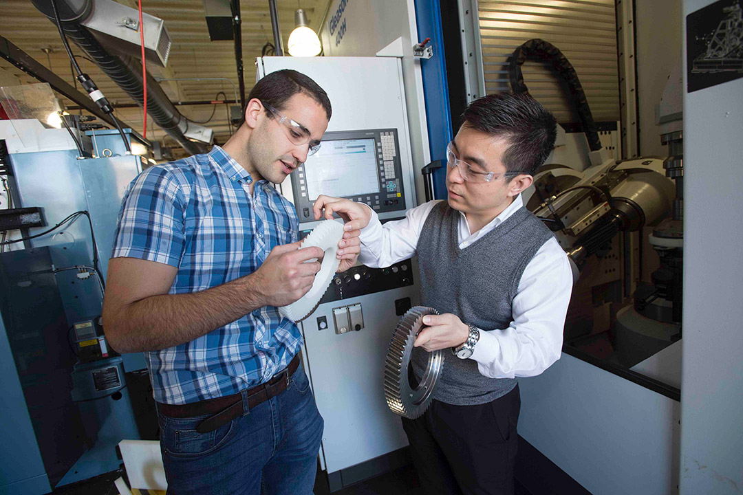 professor and student looking at large metal and plastic gears.