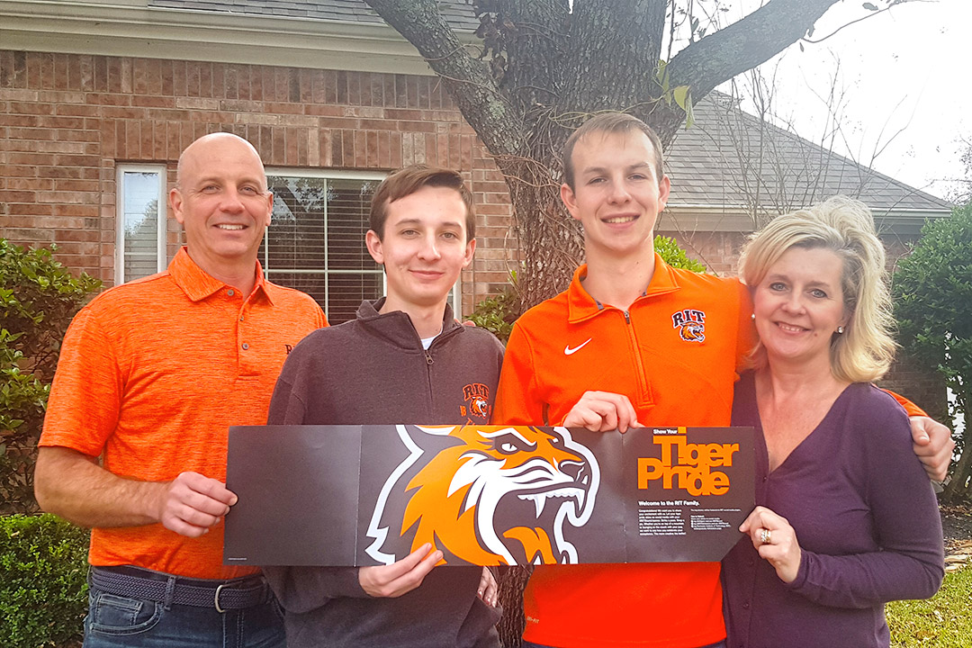 family of four holding an RIT Tiger Pride banner.