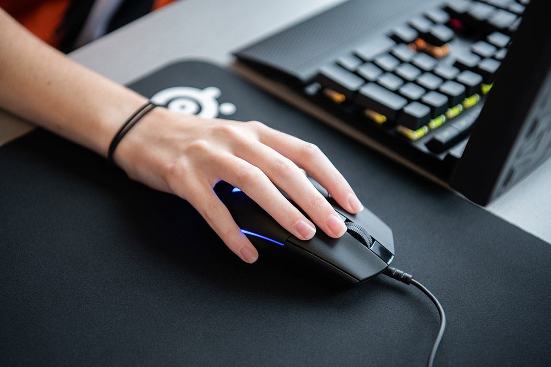 hand on computer mouse next to laptop.