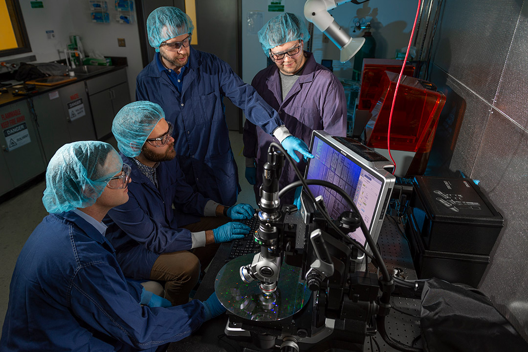 four researchers looking at computer that's analyzing a quantum photonics wafer.