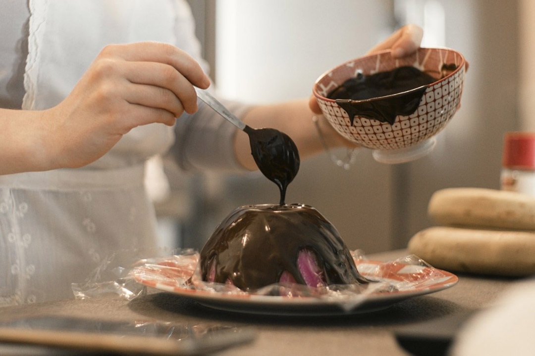 student drizzling melted chocolate over a dome form.