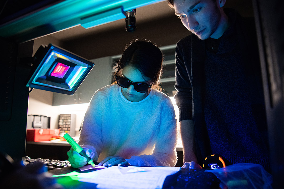 student wearing sunglasses highlights paper under colorful light.