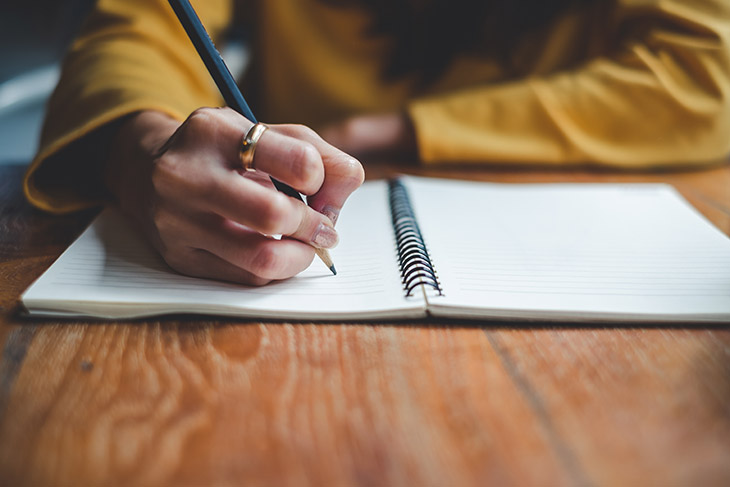 person writing in spiral-bound notebook.