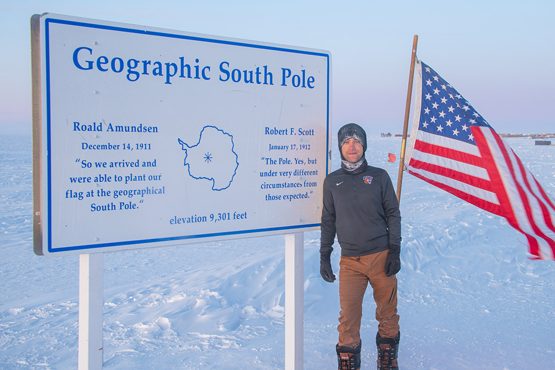 man standing at the geographic south pole with an American flag.