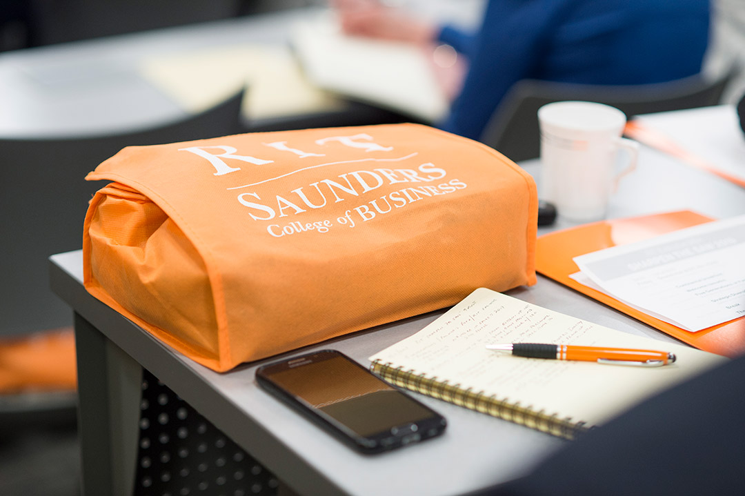 table with phone, pad of paper, pen, and orange reusable bag.