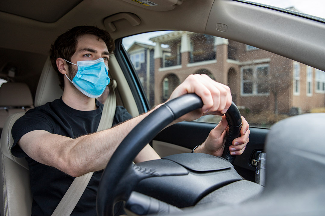 student driving car while wearing face mask.