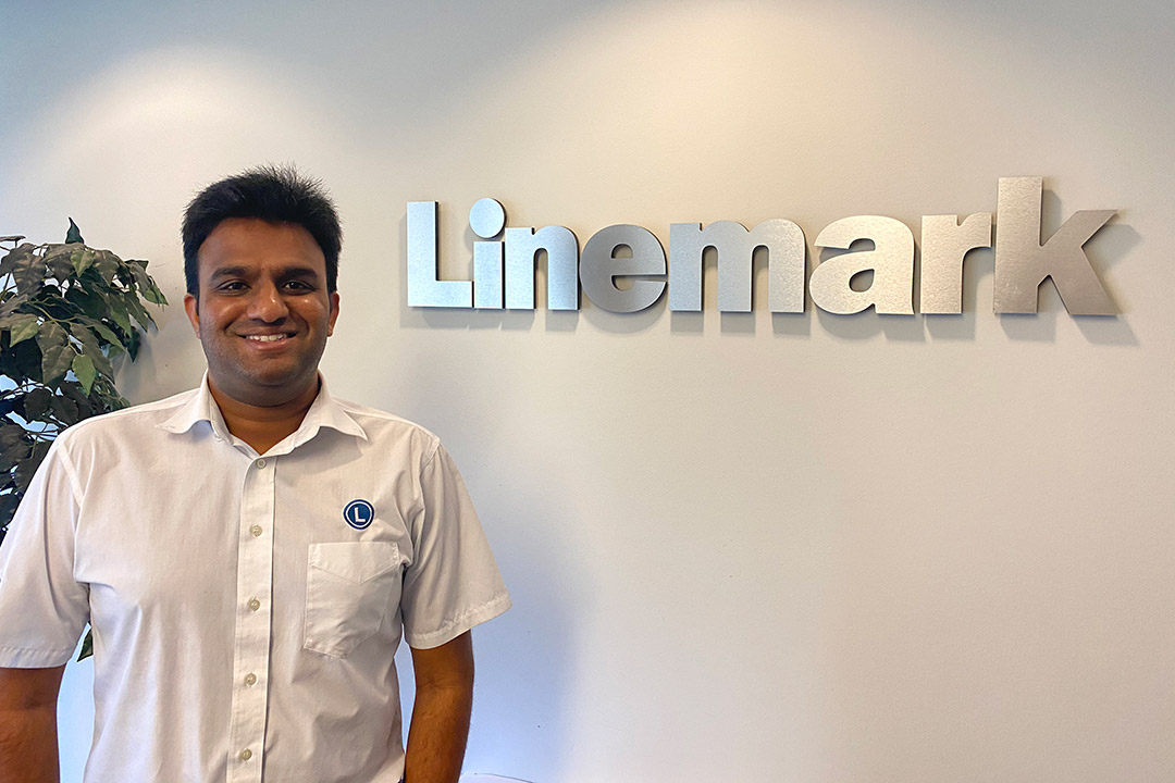 employee standing next to Linemark logo on wall.