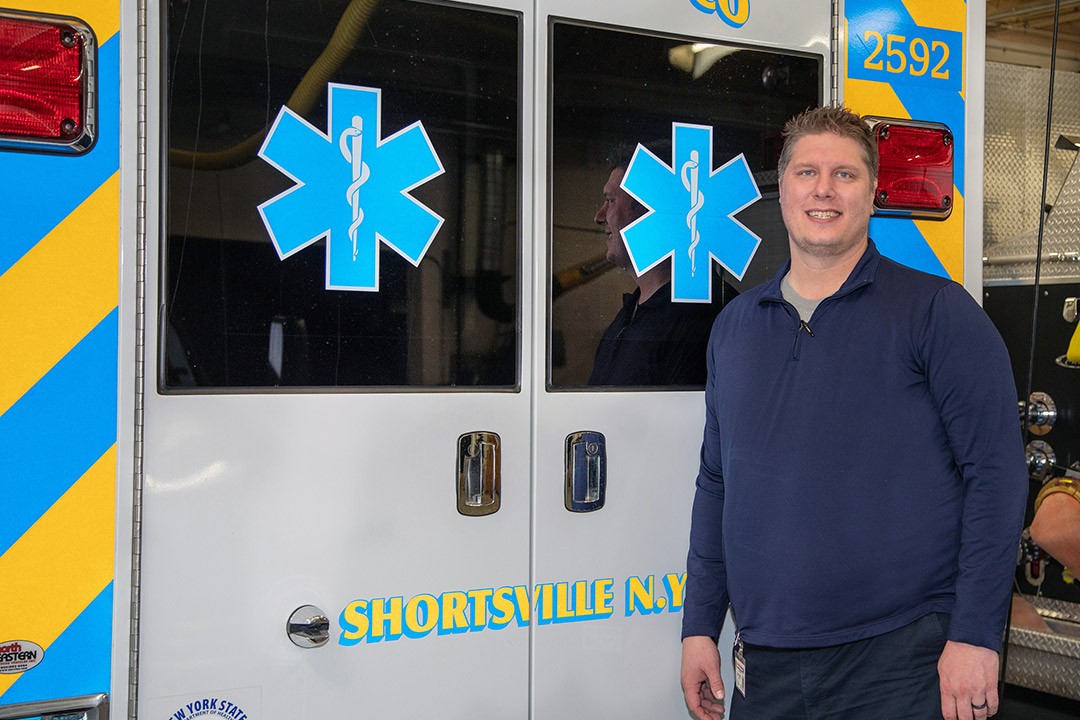 student posing behind Shortsville, N.Y. ambulance.