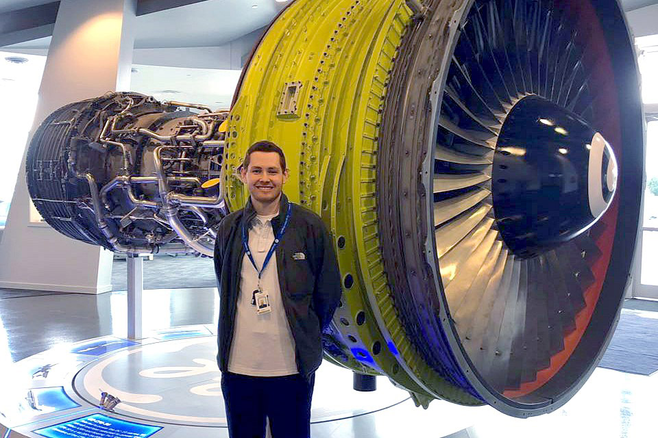 student standing in front of huge jet engine.