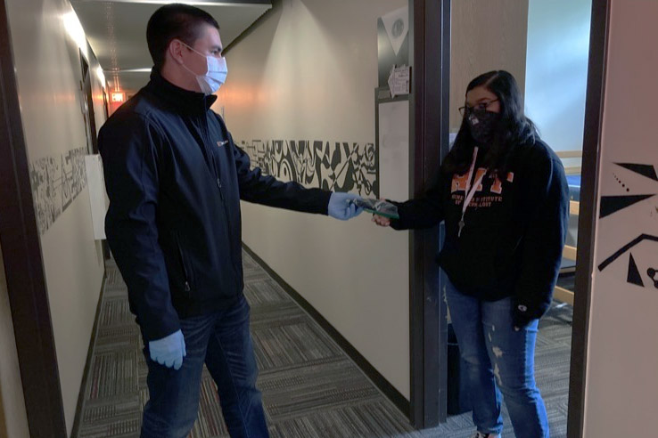 staff person handing mask to student in dorm.