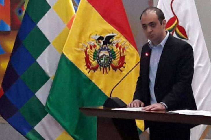 man speaking at podium next to the Bolivian flag.