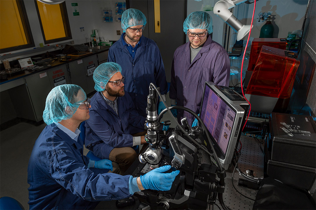 Four scientists analyzing quantum photonics wafer.