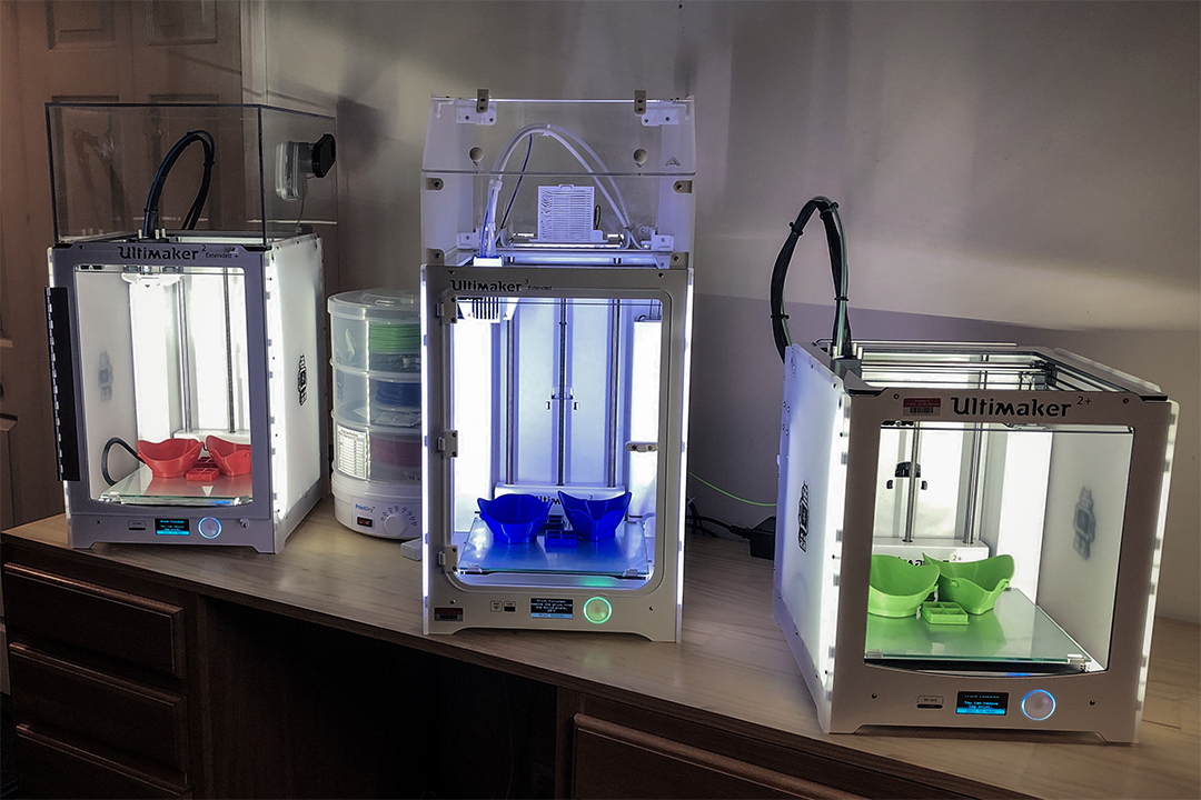 Three 3D printers creating PPE equipment.