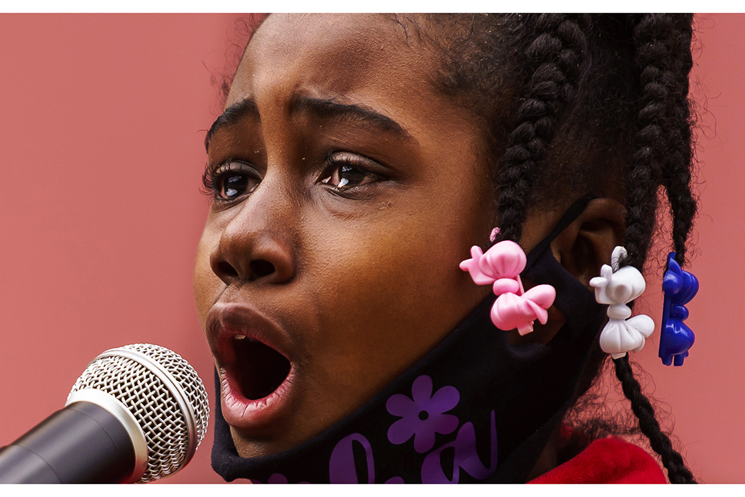 A girl stands behind a microphone, fighting back tears.