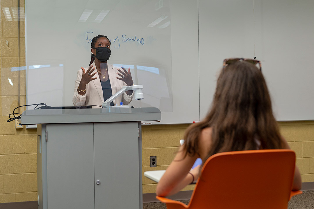 professor teaching from podium behind a plexiglas barrier.