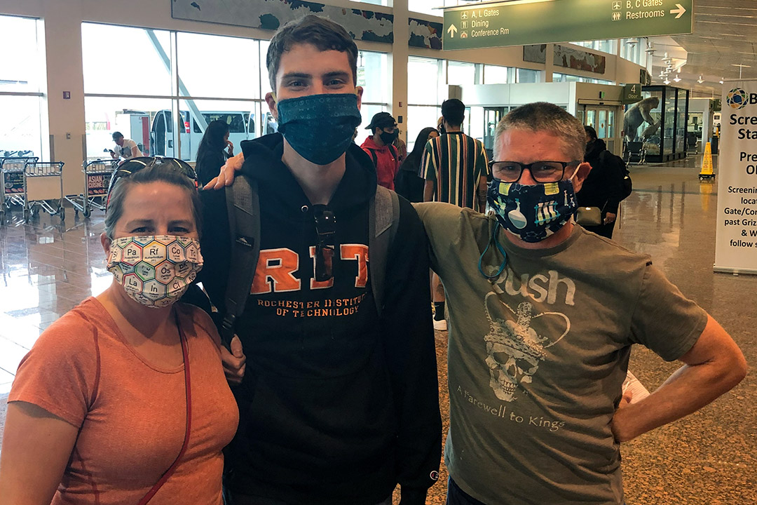 family of three standing in an airport wearing face masks.