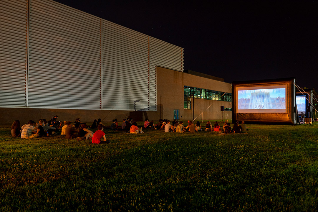 students seated on a lawn attending an outdoor movie at night.