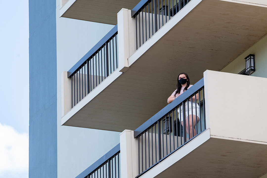student wearing a mask standing on a hotel balcony.