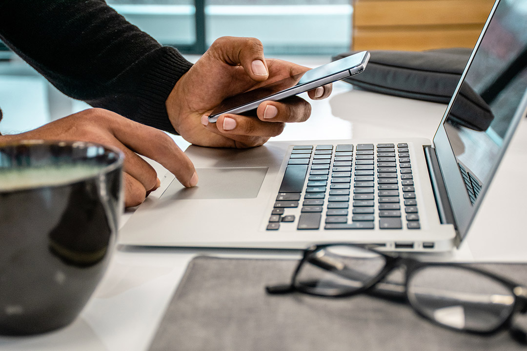 set of hands holding cellphone and operating a laptop computer.