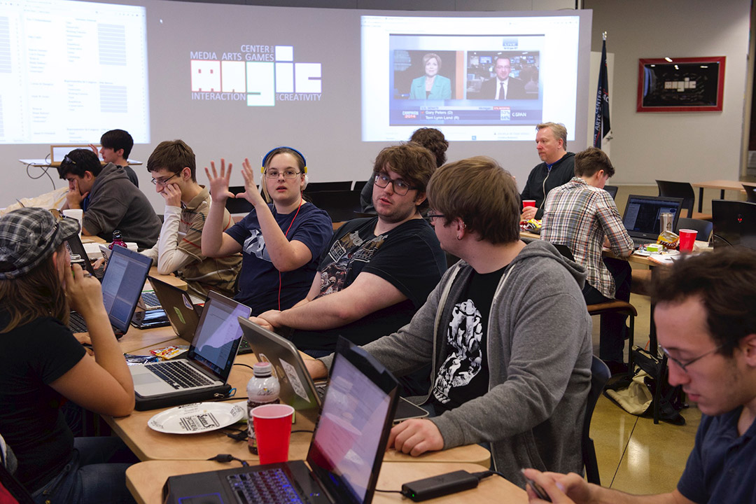 Students gathered at tables working together with computers.