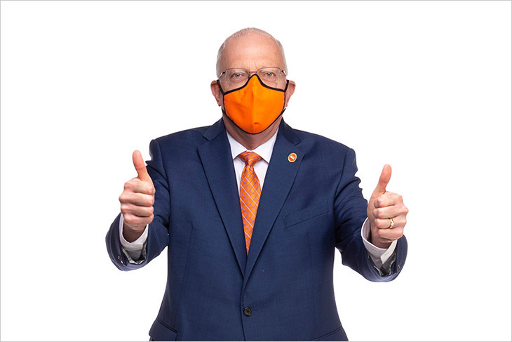 President Munson wearing an orange face mask and giving two thumbs up.