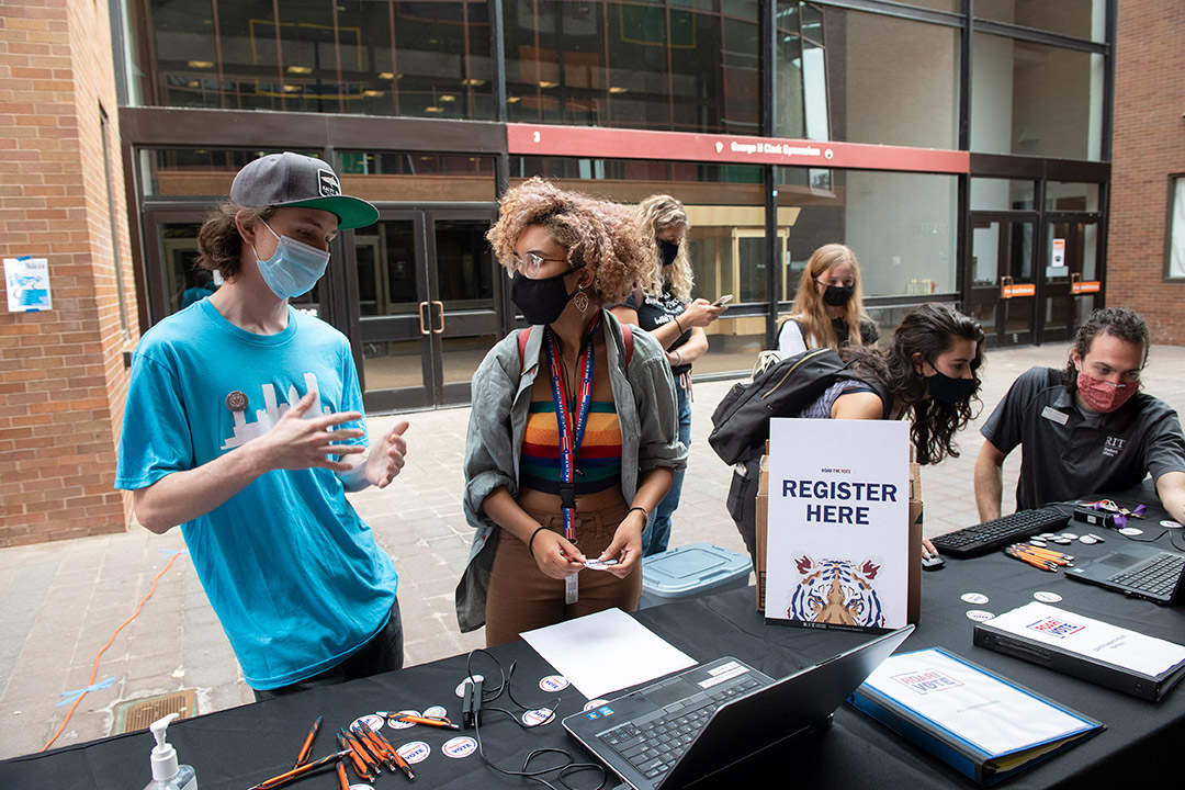 students and staff members at a table outdoors learning about voting registration. 