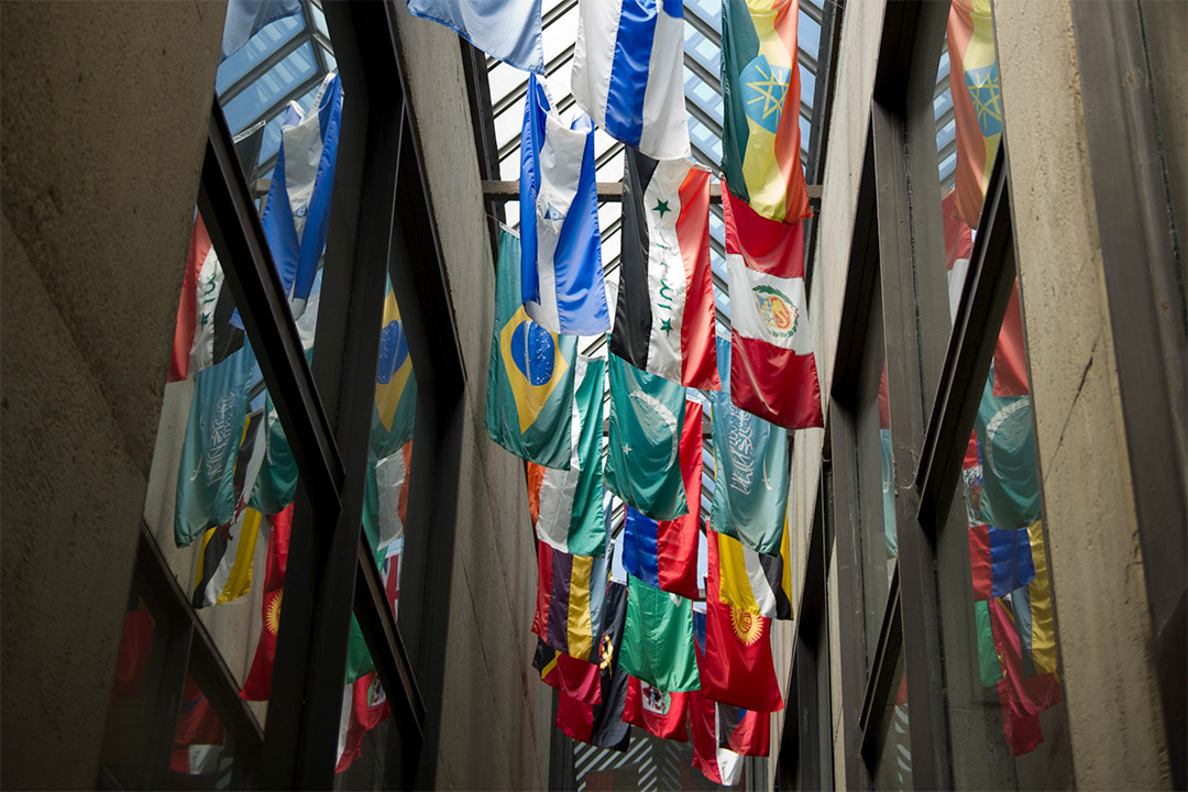 flags of different countries hanging from the glass ceiling in a hallway.