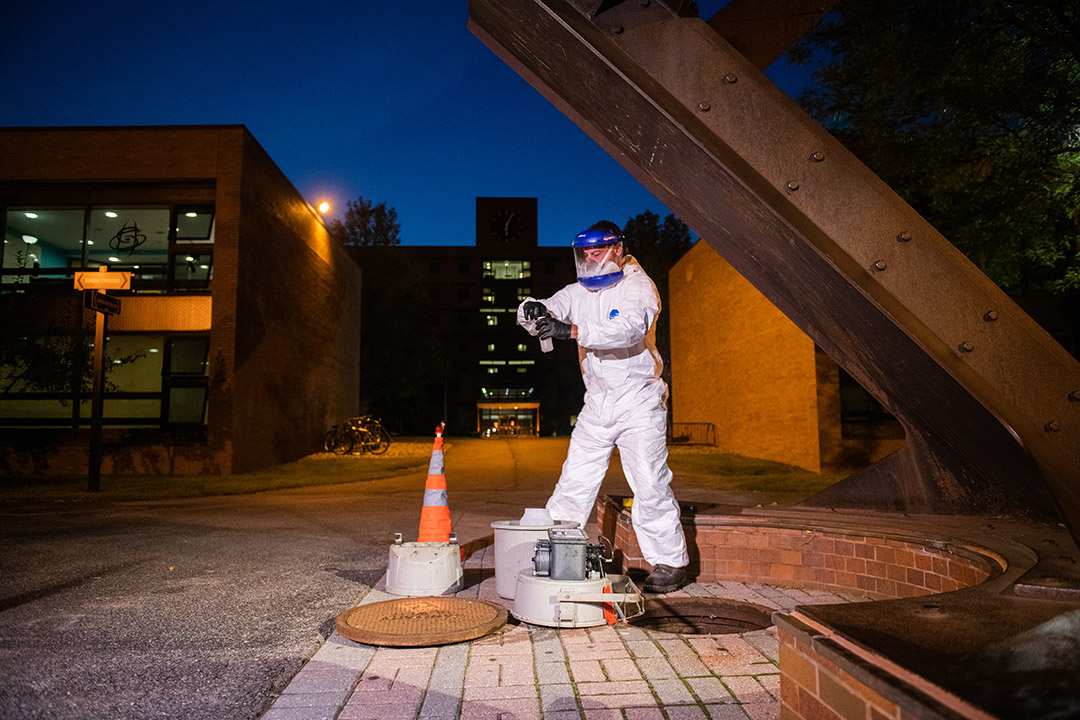 worker taking sample of wastewater from an open sewer access point.