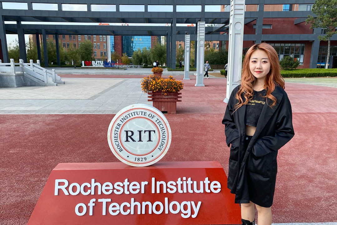 student standing next to RIT logo and sign outside in China.