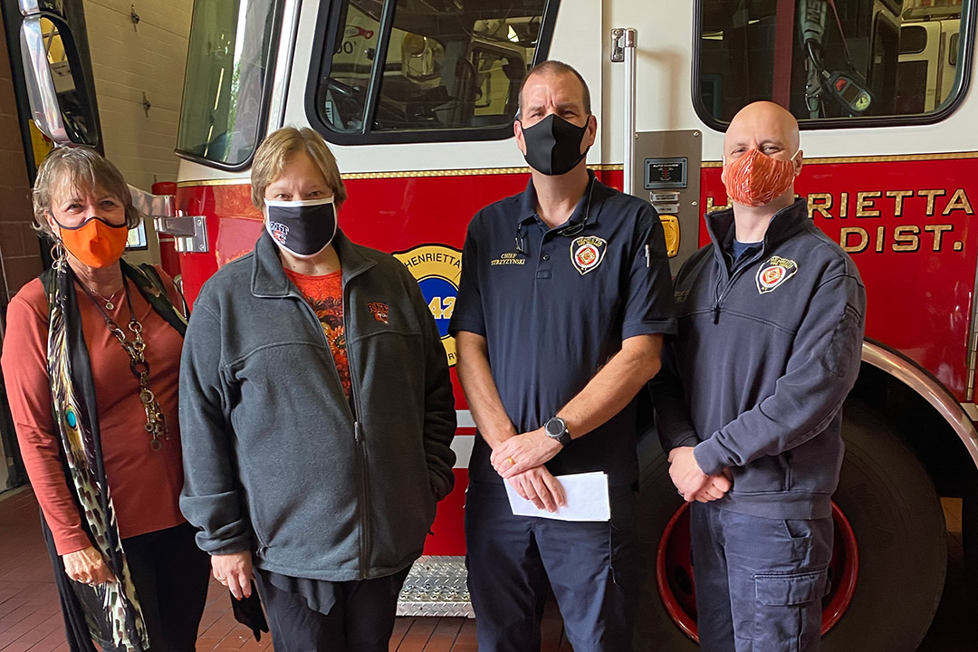 four people wearing masks standing next to a firetruck.