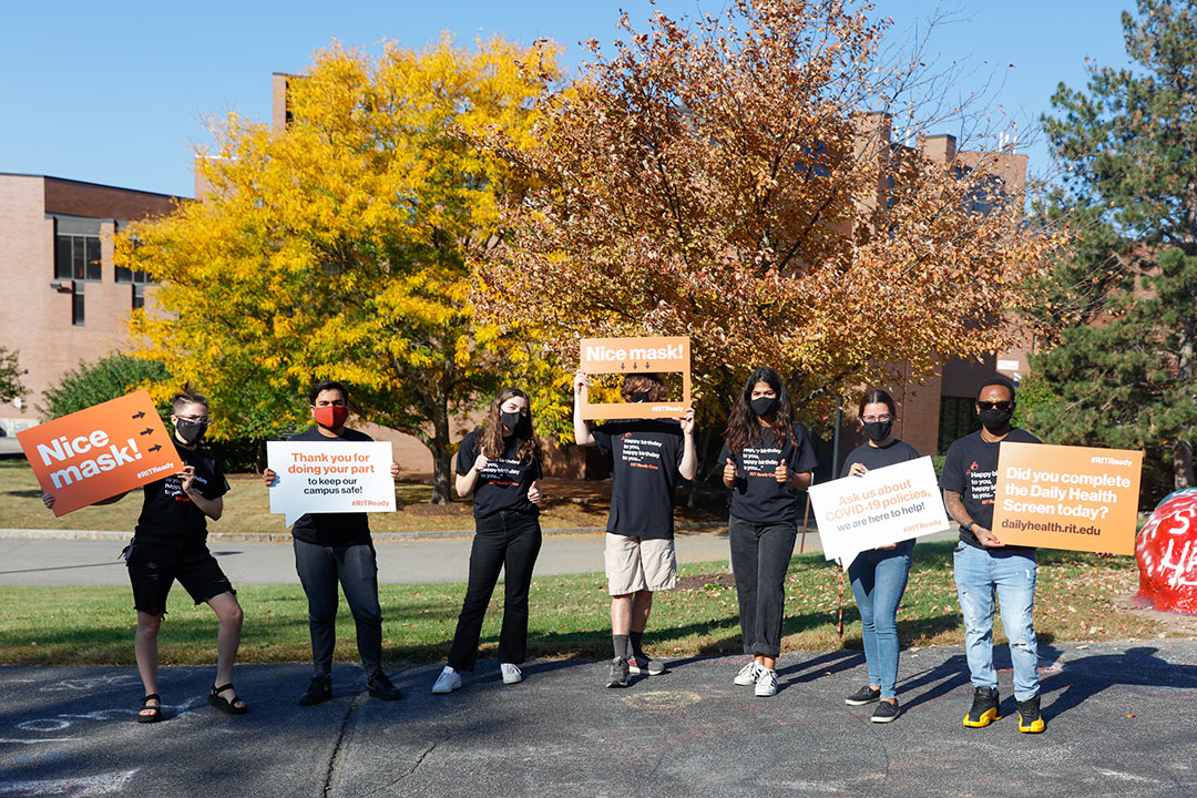 seven students holding large signs related to COVID-19 procedures on campus.
