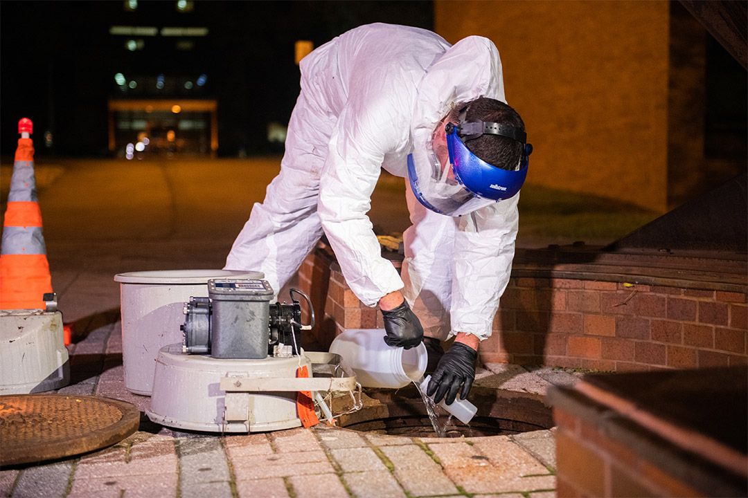 worker taking sample of wastewater from an open sewer access point.